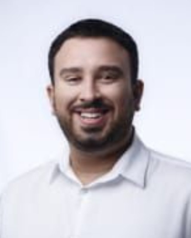 Retrato oficial de Antoniel Holanda, sorrindo, de camisa branca, em fundo claro