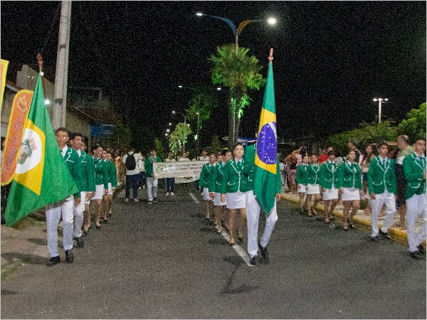 Estudantes de verde e branco desfilam à noite com as bandeiras do Brasil e do Ceará